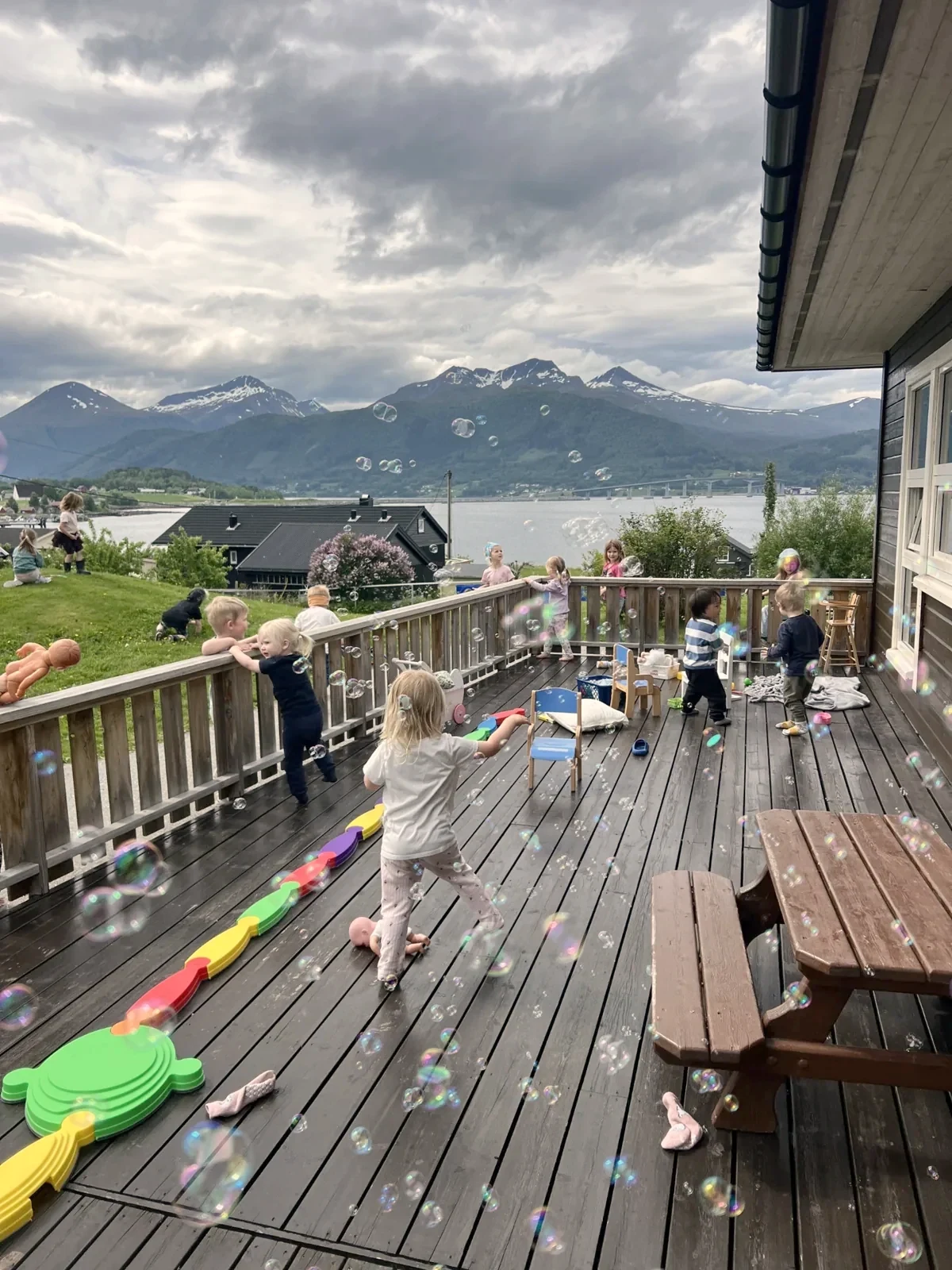Born leikar med såpebobler på terrassen med utsikt over fjord og fjell
